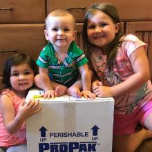 Young girl, toddler girl and baby boy sitting around a box