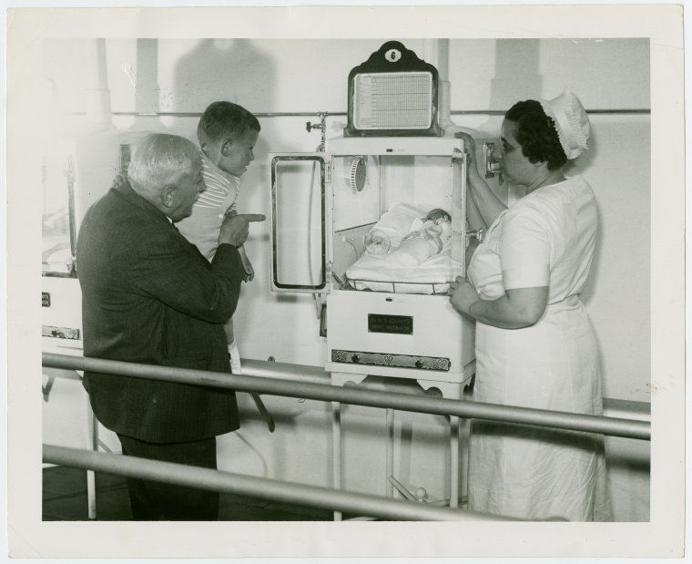 Martin and Hildegarde Couney with boy looking at baby in incubator 
