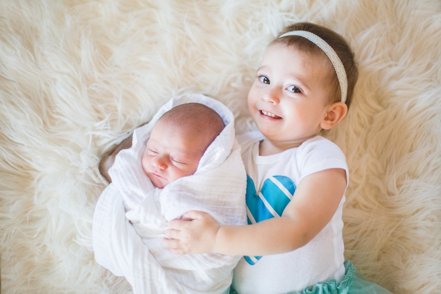 Toddler sister and infant brother laying on furry backdrop