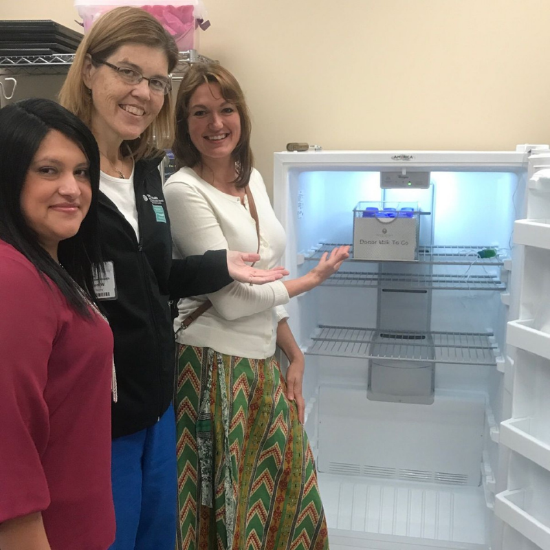 Three women standing next to open upright freezer