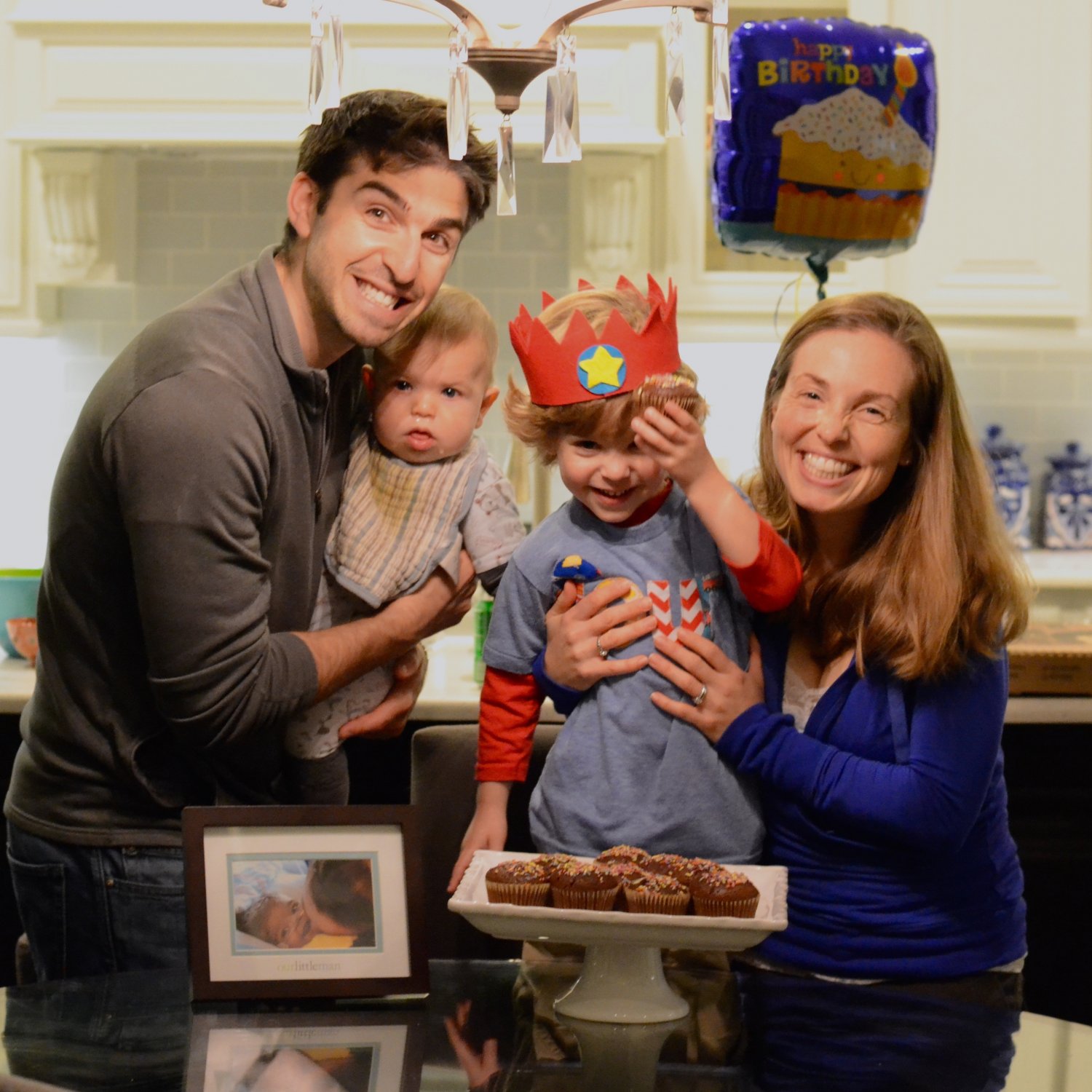 Father holding infant son, mother holding toddler son, celebrating toddler's birthday