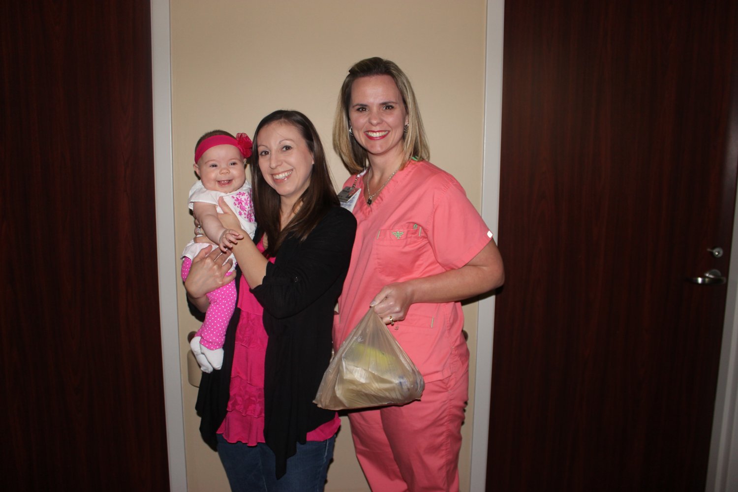 Mother holding baby, standing with nurse holding bag of frozen breastmilk