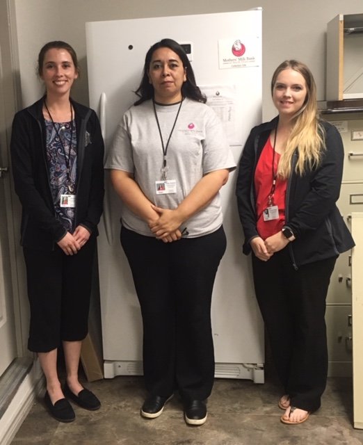 Three women standing next to upright freezer