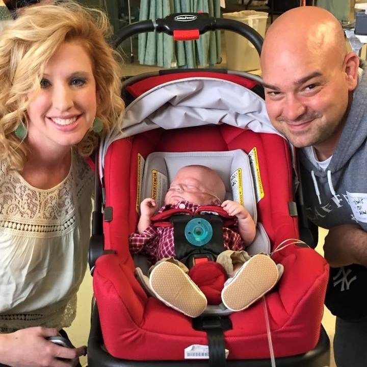 Mother and father posed around infant son, in carrier