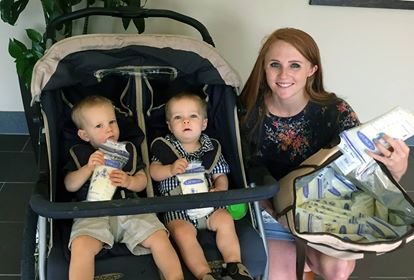 Mother holding a bag of breastmilk, crouching next to her twin boys in their stroller