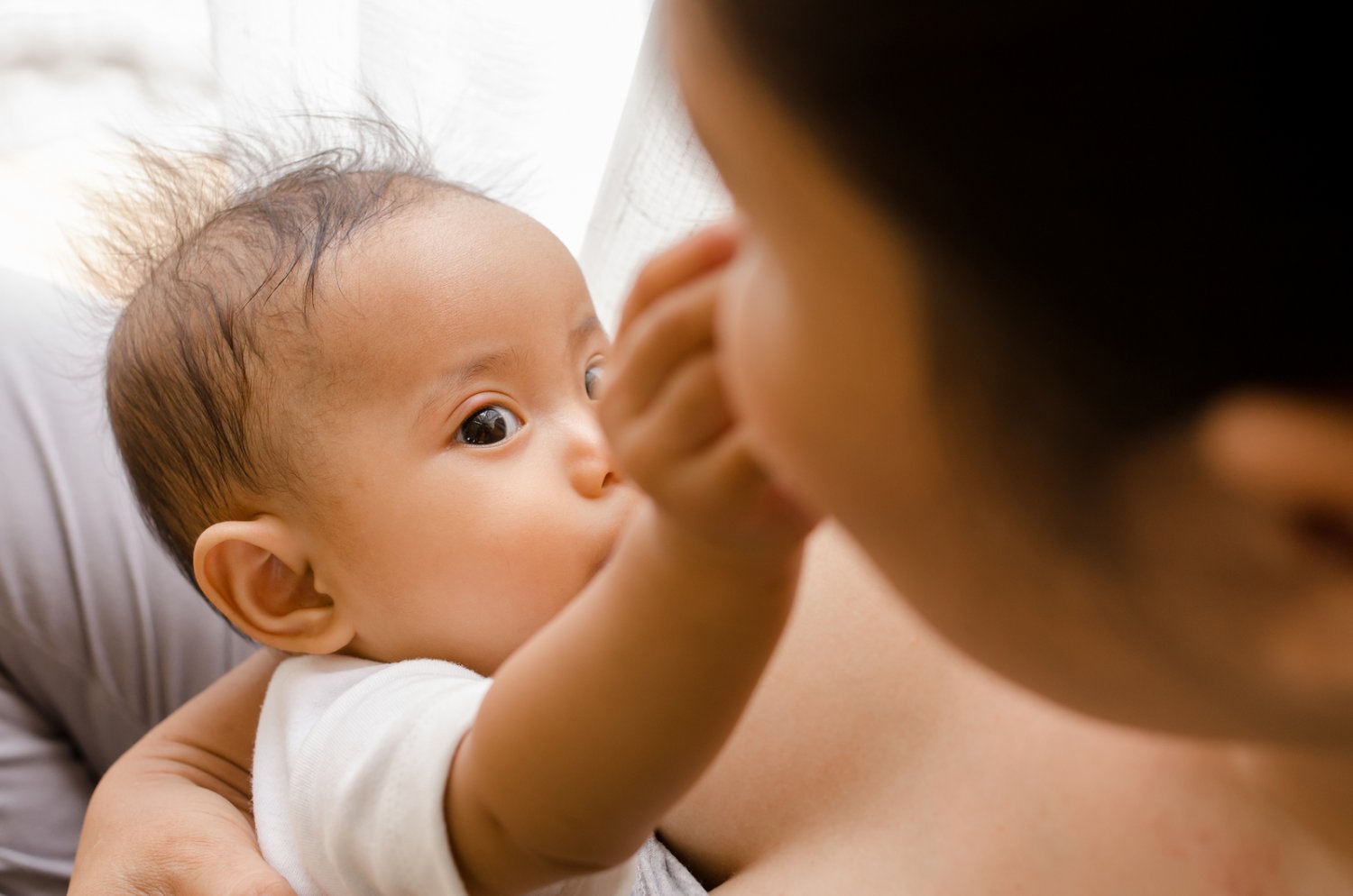 Breastfeeding baby reaching for mother's nose