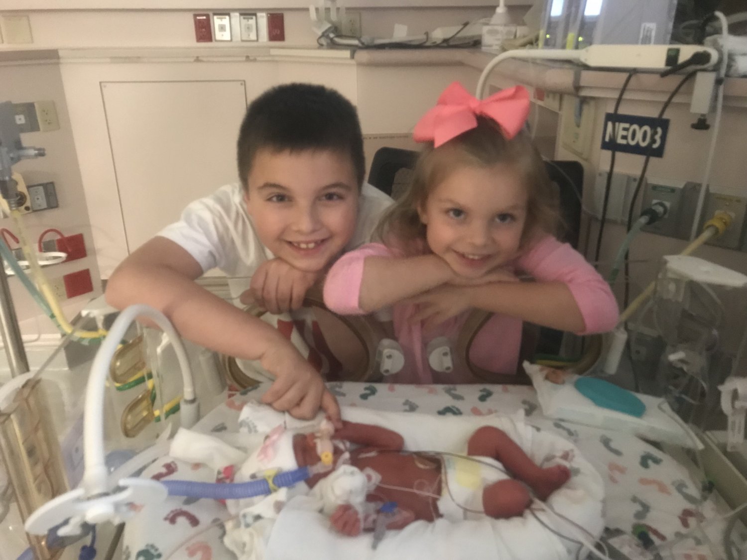 Brother and sister standing next to premature infant sister's bassinet