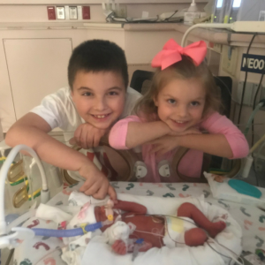 Brother and sister standing next to premature infant sister's bassinet